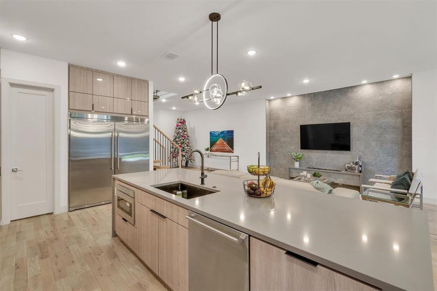 Kitchen with sink, built in appliances, light wood-type flooring, light brown cabinetry, and pendant lighting