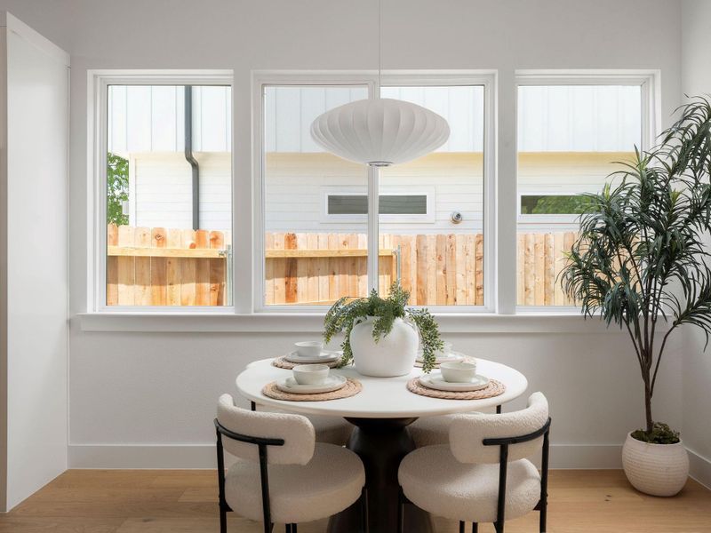 A well-lit dining area offers a cozy spot for meals with serene backyard views.