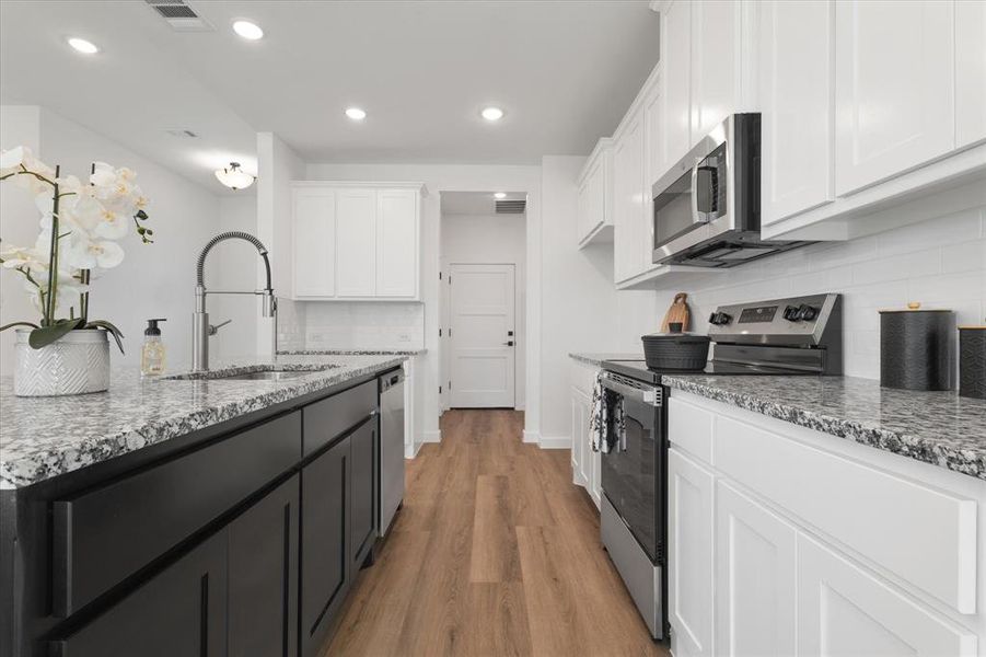 Kitchen with appliances with stainless steel finishes, light hardwood / wood-style floors, white cabinetry, light stone countertops, and sink
