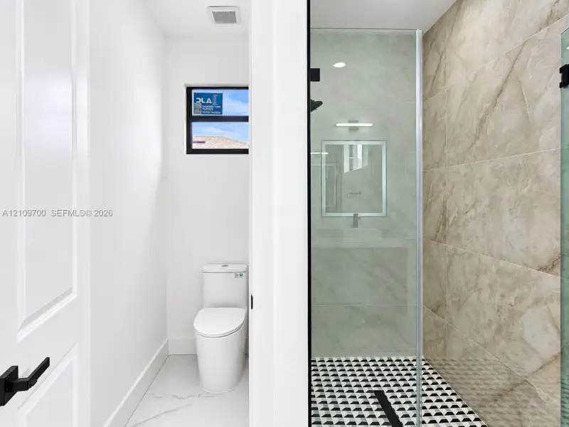 Bathroom featuring a walk-in glass-enclosed shower, large-format tile wall surround, patterned geometric floor tile, one-piece dual-flush toilet, and matte black hardware
