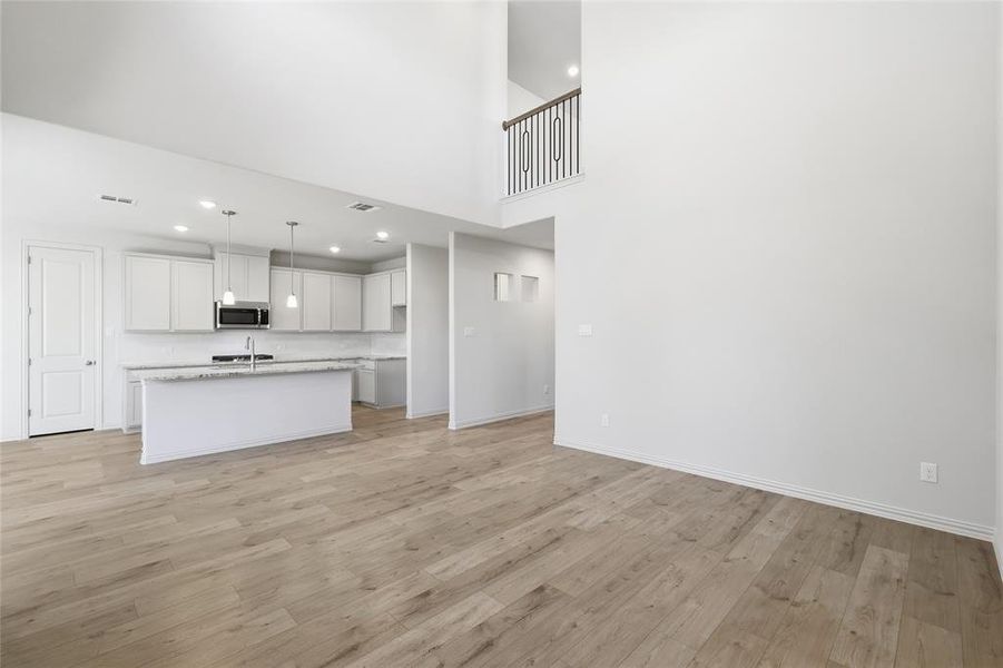 Unfurnished living room with recessed lighting, light wood-style flooring, and a towering ceiling