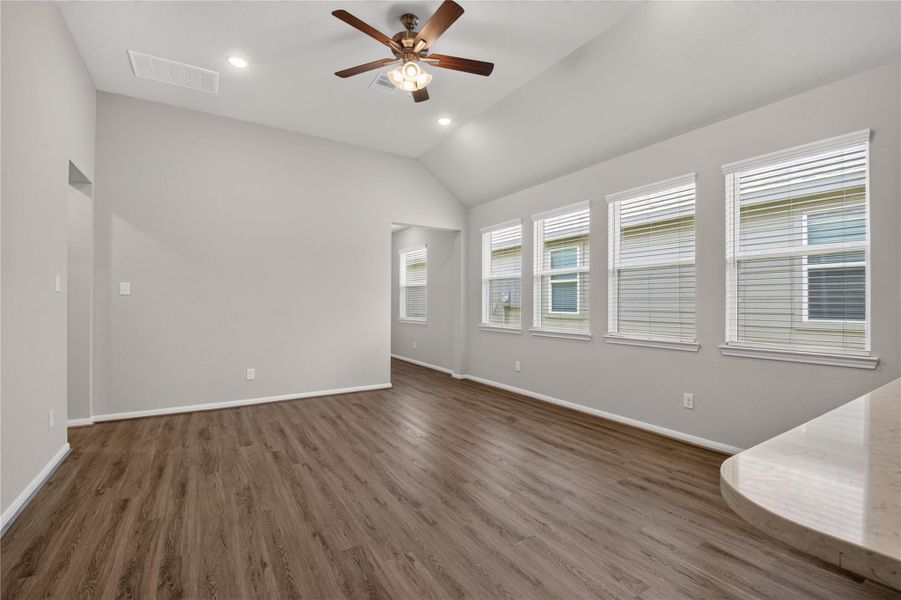 This photo showcases a spacious living area with high ceilings, wood-like flooring, and neutral walls. It features an open layout with a view into a modern kitchen, complete with a breakfast bar. Ample natural light streams through multiple windows, and a ceiling fan adds comfort. The space leads to adjacent rooms, offering convenience and functionality. This photo showcases a spacious living area with high ceilings, wood-like flooring, and neutral walls. It features an open layout with a view into a modern kitchen, complete with a breakfast bar. Ample natural light streams through multiple windows, and a ceiling fan adds comfort. The space leads to adjacent rooms, offering convenience and functionality.
