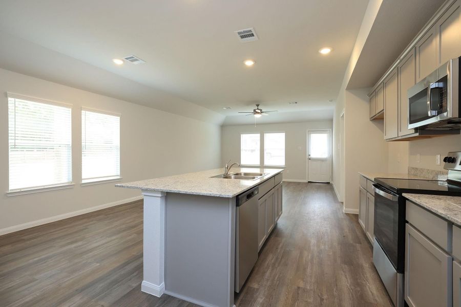 Sleek cabinetry and a large island with a sink make your culinary adventures oh such fun! Natural light streams through the windows, enhancing the spaciousness of the room.
