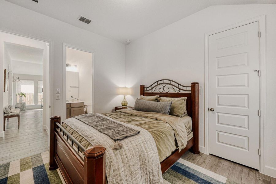 Bedroom featuring light wood-style floors, ensuite bath, and vaulted ceiling