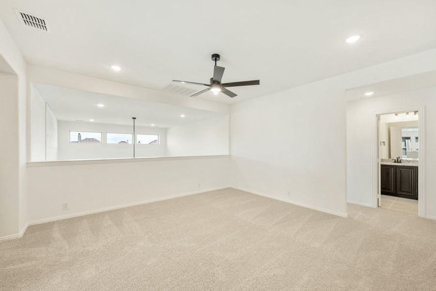 Spacious bedroom with beige carpet, ceiling fan, and doorway leading to an ensuite bathroom