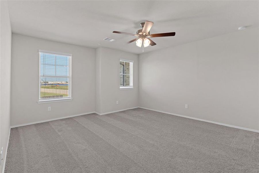 This primary bedroom features neutral walls and carpeting, two large windows for natural light, and a ceiling fan with lighting. Ready for personal touches.