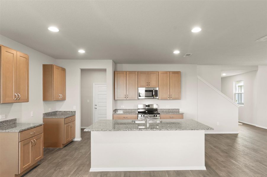 Kitchen featuring appliances with stainless steel finishes, wood finished floors, a kitchen island with sink, recessed lighting, and light stone countertops