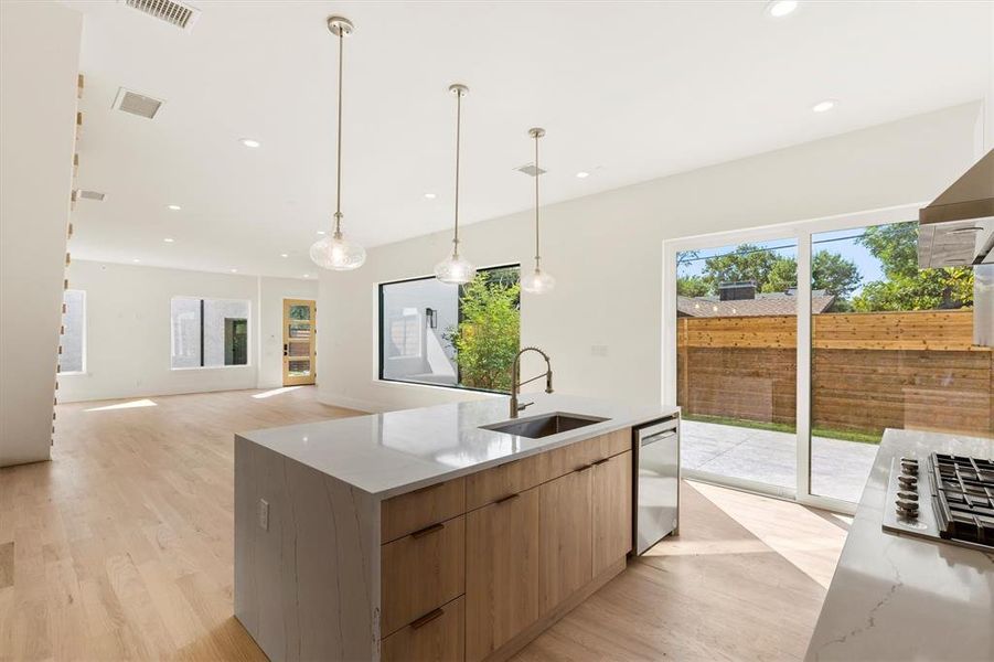 Kitchen with light stone countertops, stainless steel appliances, sink, hanging light fixtures, and light hardwood / wood-style flooring