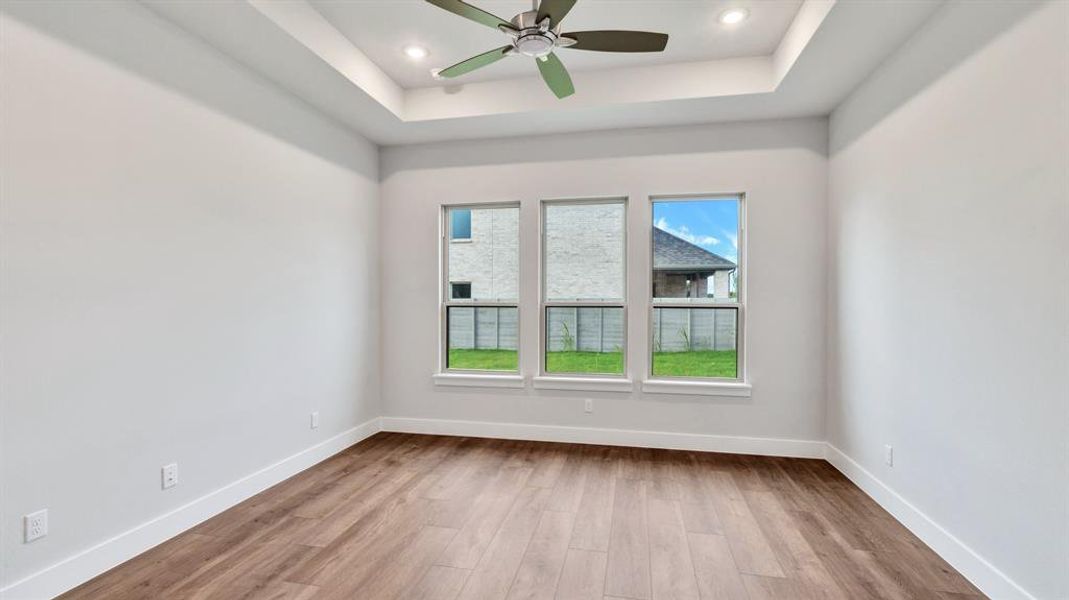 Spare room with ceiling fan, light hardwood / wood-style floors, and a raised ceiling