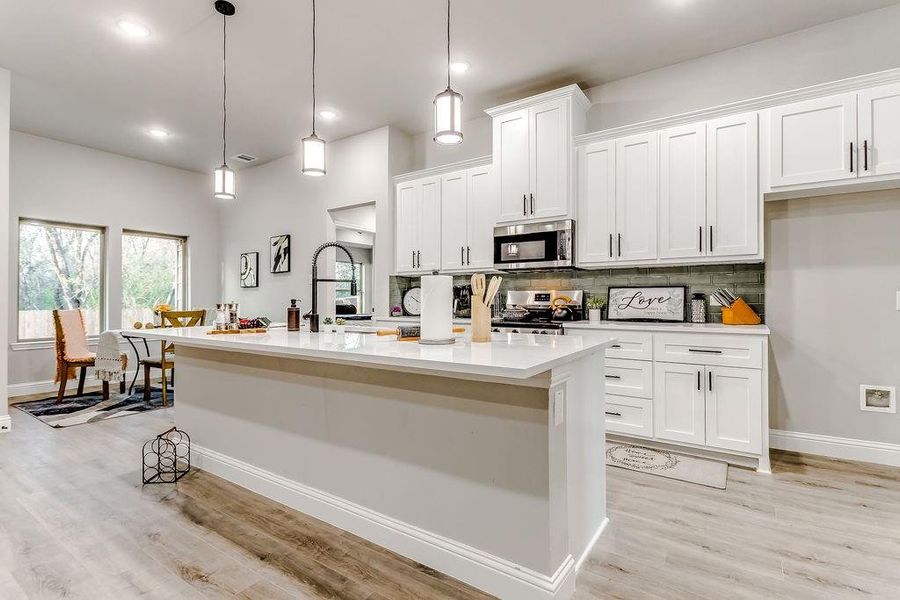 Kitchen with appliances with stainless steel finishes, light wood-type flooring, pendant lighting, a center island with sink, and white cabinetry