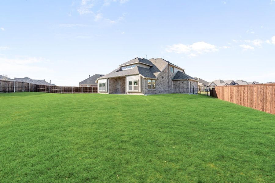 Brick home rear exterior with large grassy backyard enclosed by wood privacy fence