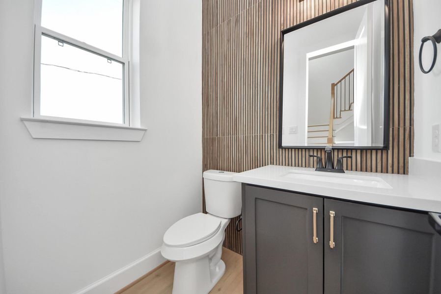 A sleek, modern bathroom featuring a vertical wood accent wall, black vanity with a white countertop, and a large mirror. Natural light from the window enhances the bright, contemporary aesthetic.
