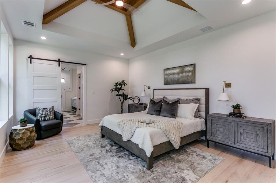 Bedroom with a barn door, connected bathroom, beamed ceiling, and hardwood / wood-style flooring