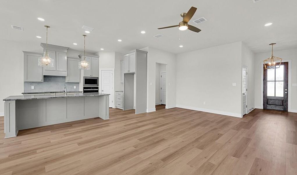 Kitchen featuring pendant lighting, decorative backsplash, a chandelier, light wood-style floors, and an island with sink