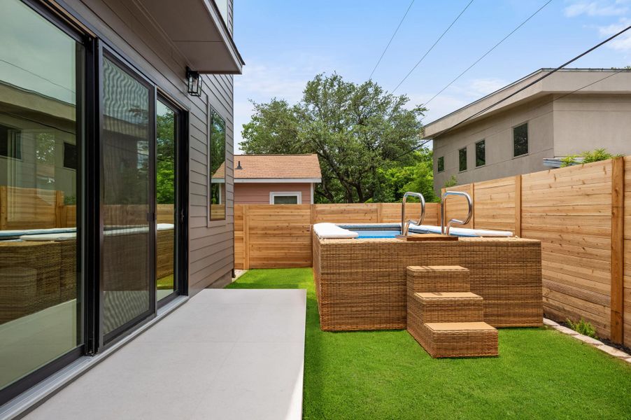 A private backyard oasis features a modern hot tub and green space, perfect for relaxing.