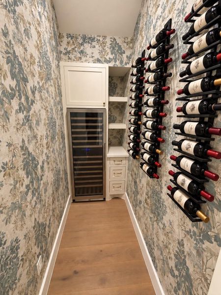 Dedicated wine room with oversized wine fridge and custom built ins and wallpaper