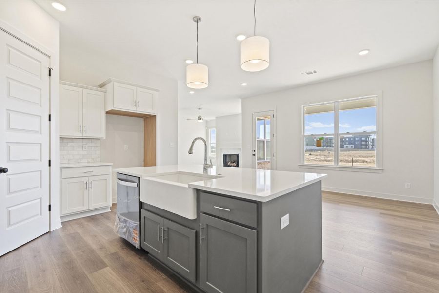 Dual tone kitchen featuring dual tone cabinets, hanging light fixtures, an island with sink, a fireplace, and dark wood-style flooring