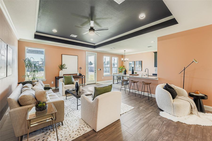 Living area featuring crown molding, a chandelier, light wood-style flooring, a ceiling fan, and a raised ceiling