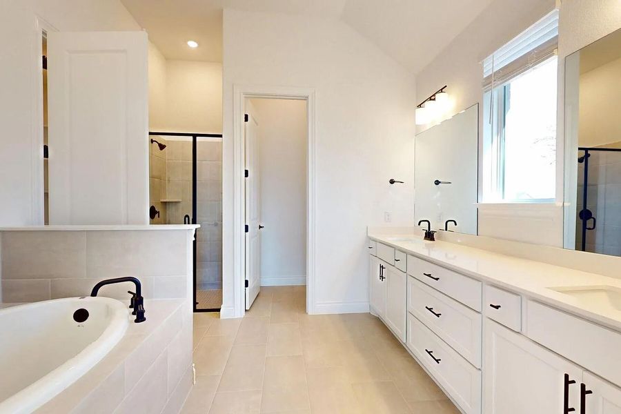 This bathroom features a soaking tub with a modern black faucet, a spacious shower with a glass enclosure, and a double vanity with two sinks and ample storage