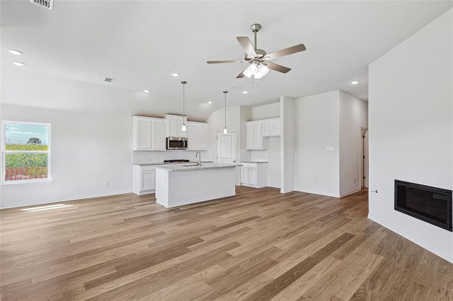 Kitchen with white cabinets, heating unit, light hardwood / wood-style floors, ceiling fan, and a center island with sink