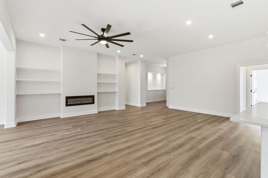 A spacious living area features recessed lighting, a modern fireplace, built-in shelving, and light wood flooring. A spacious living area features recessed lighting, a modern fireplace, built-in shelving, and light wood flooring.