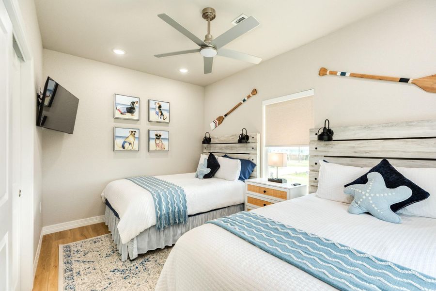 Comfortable guest bedroom features two beds, coastal-inspired décor, and abundant natural light, providing a welcoming space for family and guests.