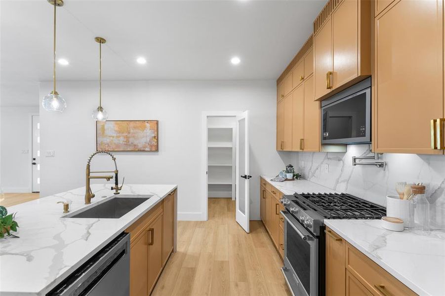 Kitchen with light stone counters, stainless steel appliances, light wood-style floors, hanging light fixtures, and decorative backsplash