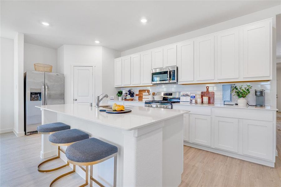 Kitchen featuring white cabinets, a center island with sink, stainless steel appliances, and light countertops