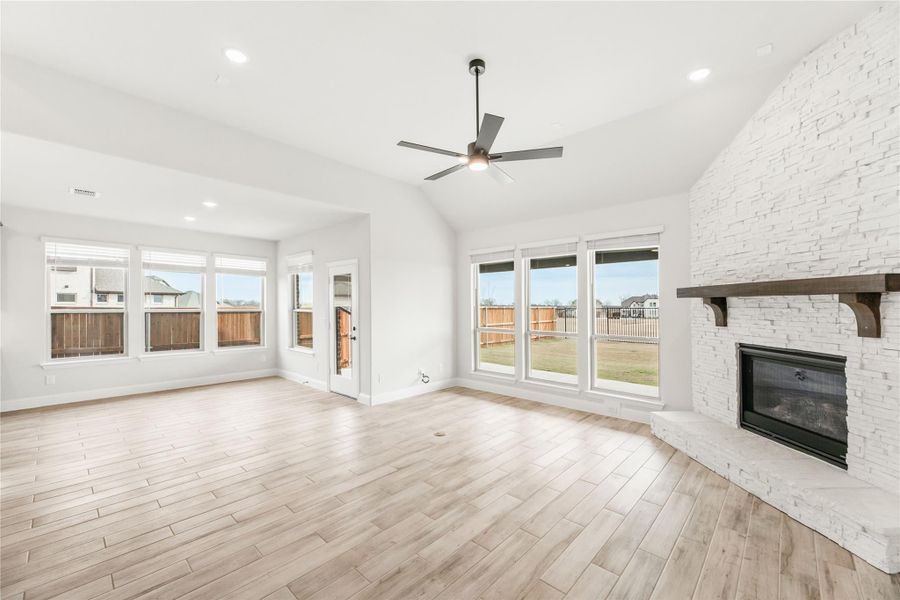 Open living room with white brick fireplace, ceiling fan, and light wood floors Open living room with white brick fireplace, ceiling fan, and light wood floors