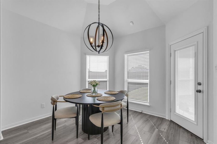 Dining space with vaulted ceiling, an inviting chandelier, and hardwood / wood-style floors