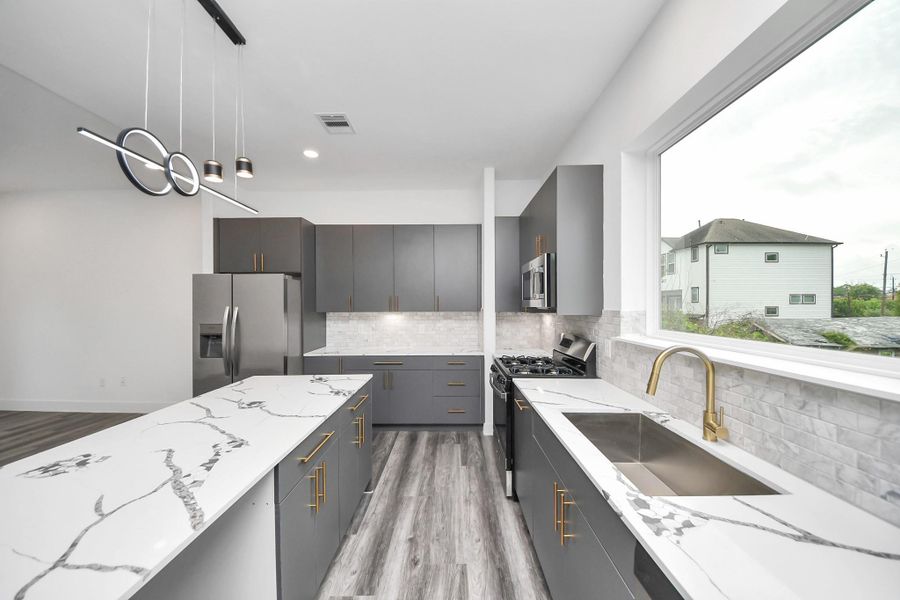 This modern kitchen features sleek gray cabinets, white quartz countertops, and a spacious island with gold hardware. Stainless steel appliances and a large window provide plenty of natural light, enhancing the open, contemporary design. This modern kitchen features sleek gray cabinets, white quartz countertops, and a spacious island with gold hardware. Stainless steel appliances and a large window provide plenty of natural light, enhancing the open, contemporary design.