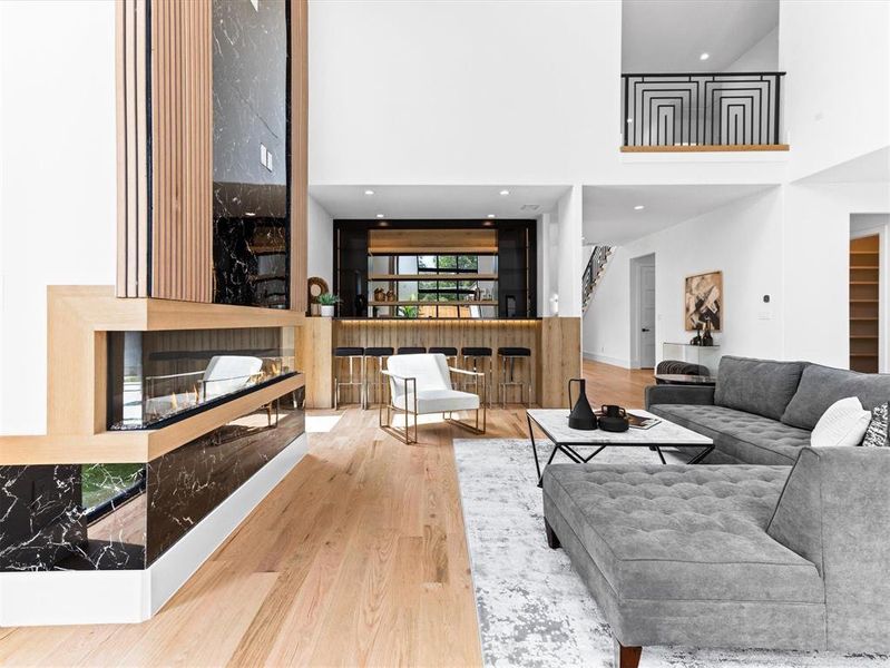 Living room featuring a multi sided fireplace, a towering ceiling, and light hardwood / wood-style floors