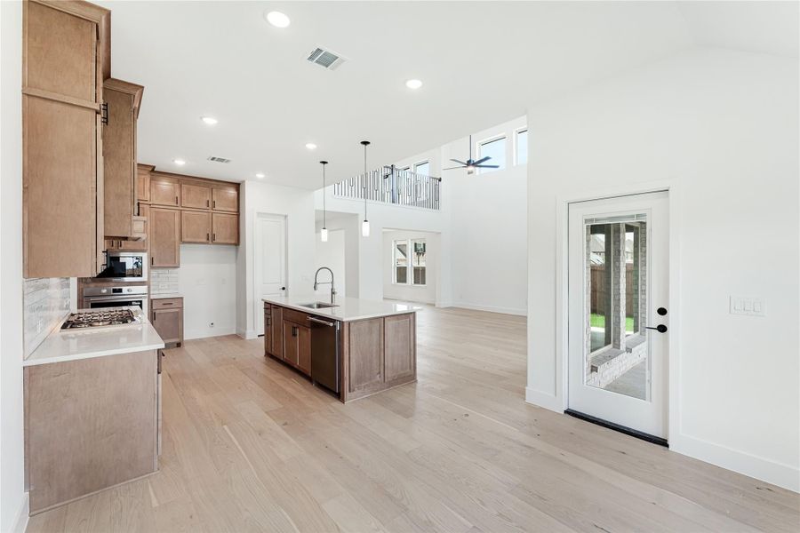 Open-concept kitchen with wood cabinets, center island, and light hardwood floors under a two-story ceiling Open-concept kitchen with wood cabinets, center island, and light hardwood floors under a two-story ceiling