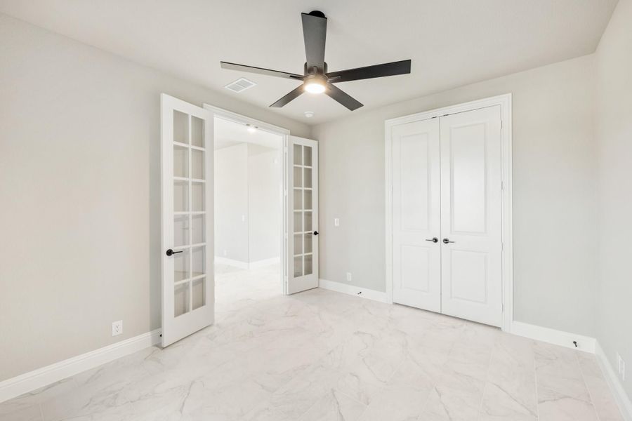 Empty bedroom with French doors, double closet, ceiling fan, and white marble tile floors