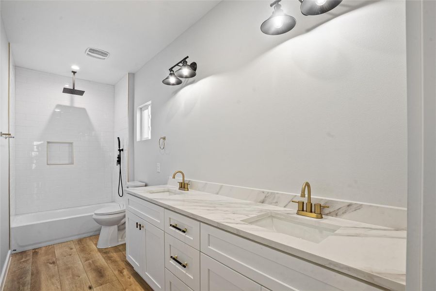 Bathroom featuring double vanity, light wood-style flooring, and a combined bath / shower with rainfall shower