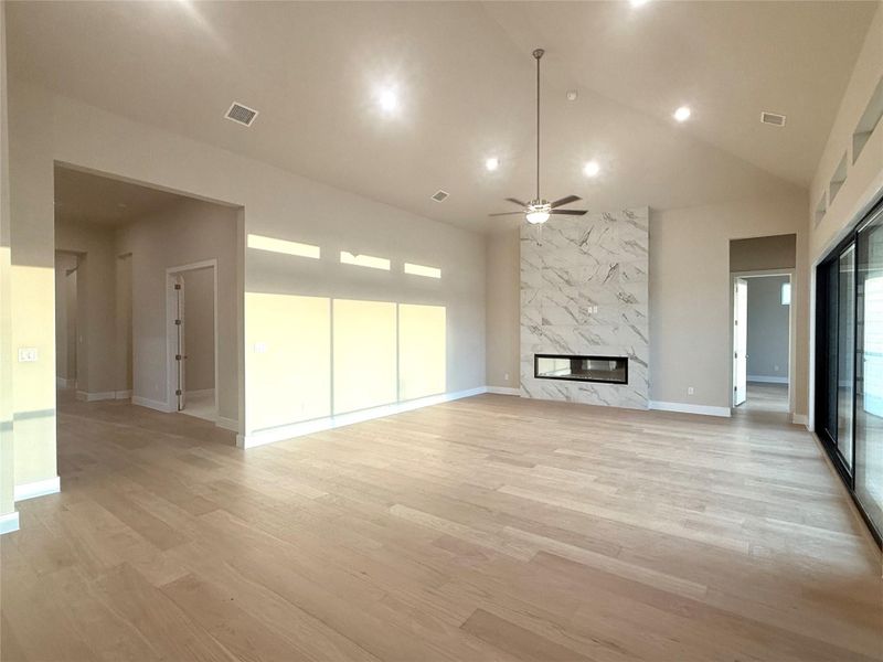 Unfurnished living room with a premium fireplace, a ceiling fan, light wood-style floors, and high vaulted ceiling