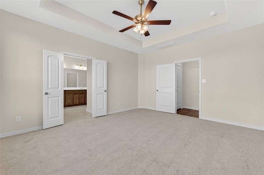 Unfurnished bedroom featuring a raised ceiling, light colored carpet, ceiling fan, and connected bathroom
