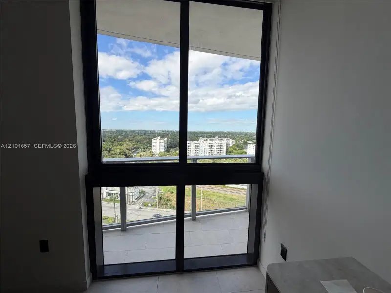Floor-to-ceiling windows with dark metal framing and a tiled balcony featuring a glass railing