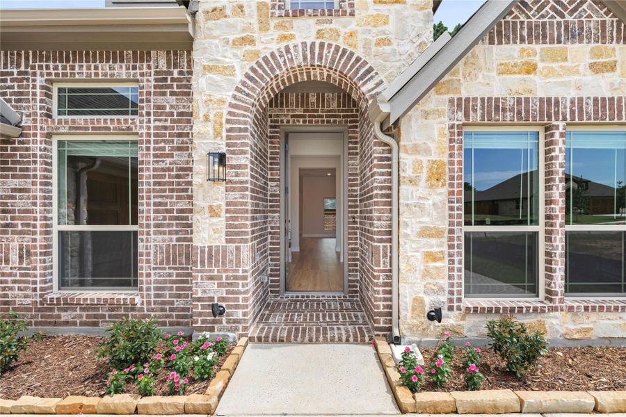 Home entrance with arched brick doorway, stone exterior, and landscaped flower beds along walkway