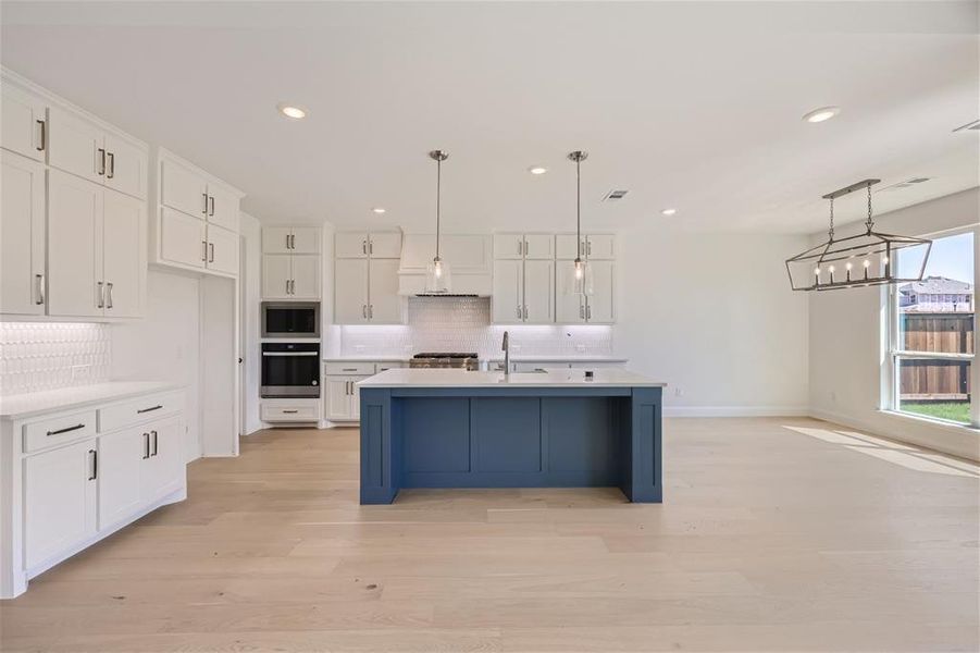 Kitchen with hanging light fixtures, an island with sink, backsplash, and appliances with stainless steel finishes