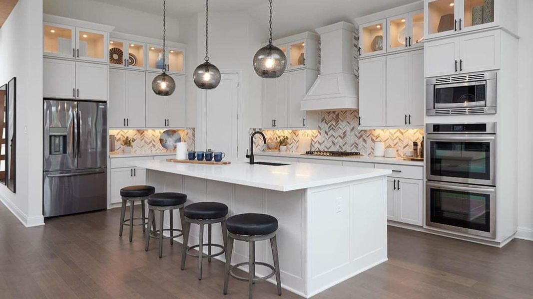 Kitchen with glass insert cabinets, stainless steel appliances, white cabinetry, decorative light fixtures, and a kitchen bar