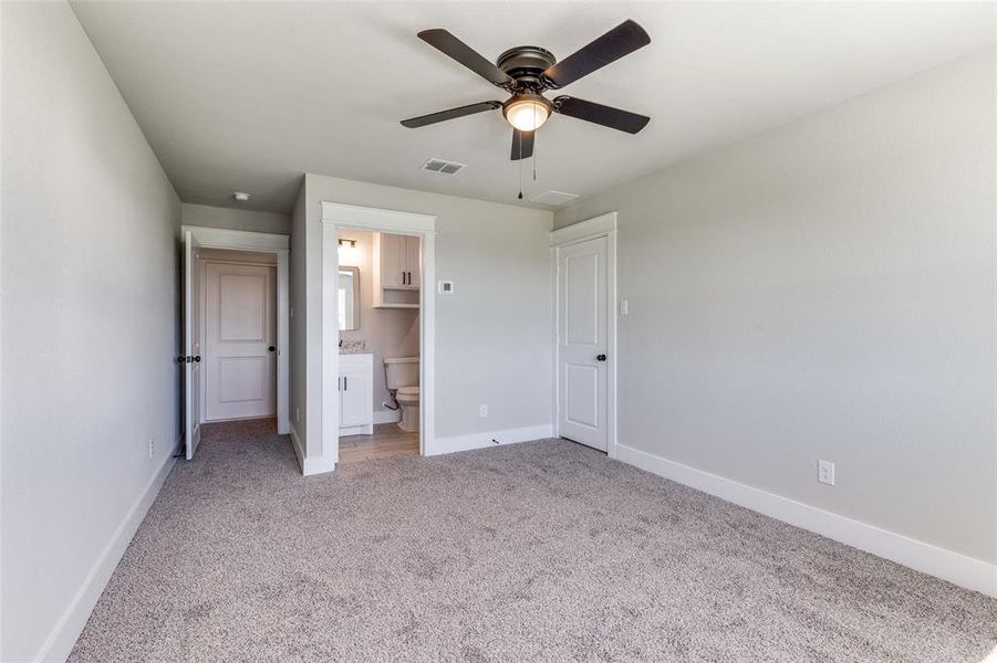 Unfurnished bedroom featuring ceiling fan, ensuite bath, and carpet