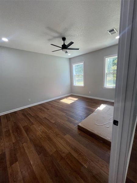 Unfurnished room featuring dark wood-style flooring, healthy amount of natural light, a textured ceiling, a ceiling fan, and recessed lighting Unfurnished room featuring dark wood-style flooring, healthy amount of natural light, a textured ceiling, a ceiling fan, and recessed lighting