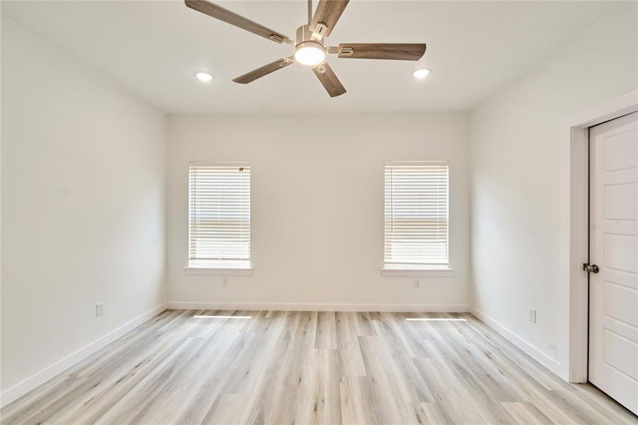 Spacious room featuring wood-finish flooring and two windows with blinds