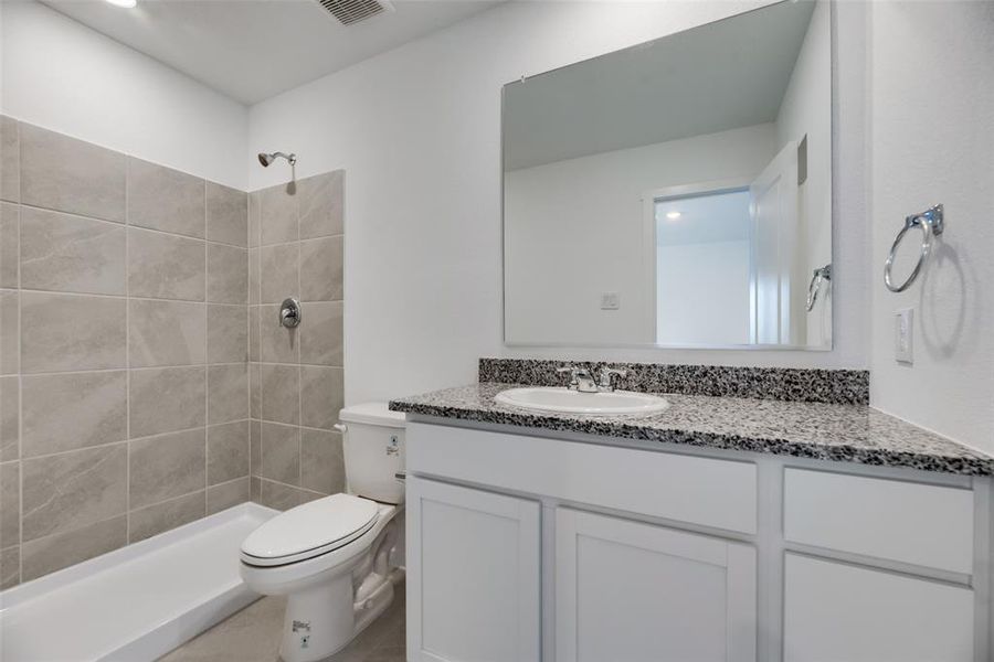 Bathroom with a tile shower, vanity, and toilet