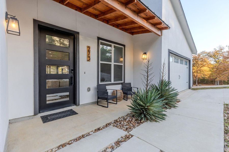 Property entrance featuring a porch, stucco siding, driveway, and an attached garage