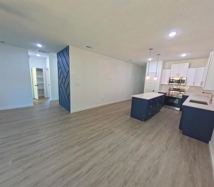 Kitchen with white cabinetry, open floor plan, stainless steel appliances, a kitchen island, and pendant lighting Kitchen with white cabinetry, open floor plan, stainless steel appliances, a kitchen island, and pendant lighting