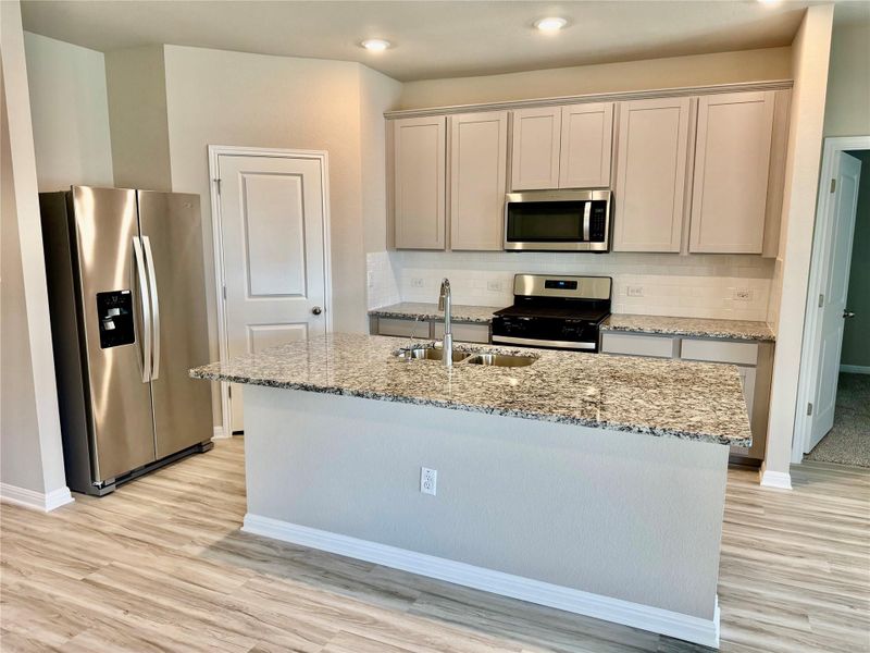 Kitchen featuring appliances with stainless steel finishes, light stone counters, backsplash, light wood-type flooring, and recessed lighting Kitchen featuring appliances with stainless steel finishes, light stone counters, backsplash, light wood-type flooring, and recessed lighting