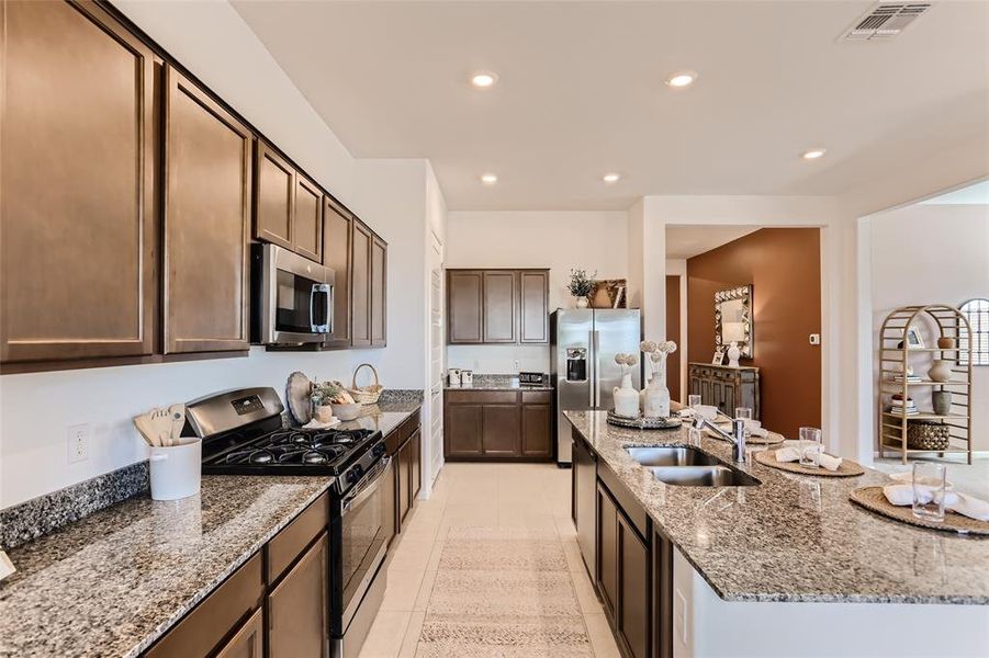 Kitchen with stainless steel appliances, light stone countertops, light tile patterned floors, recessed lighting, and dark brown cabinets