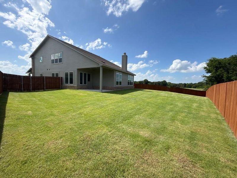 Expansive backyard featuring a manicured lawn, a full wooden privacy fence, and a covered patio area Expansive backyard featuring a manicured lawn, a full wooden privacy fence, and a covered patio area